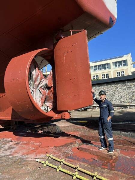 A ship's red propeller in dry dock with a technician beside it for scale